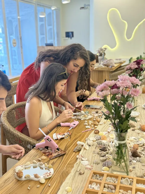 Guests decorating shell mirrors with glue guns at the long wooden table in the studio